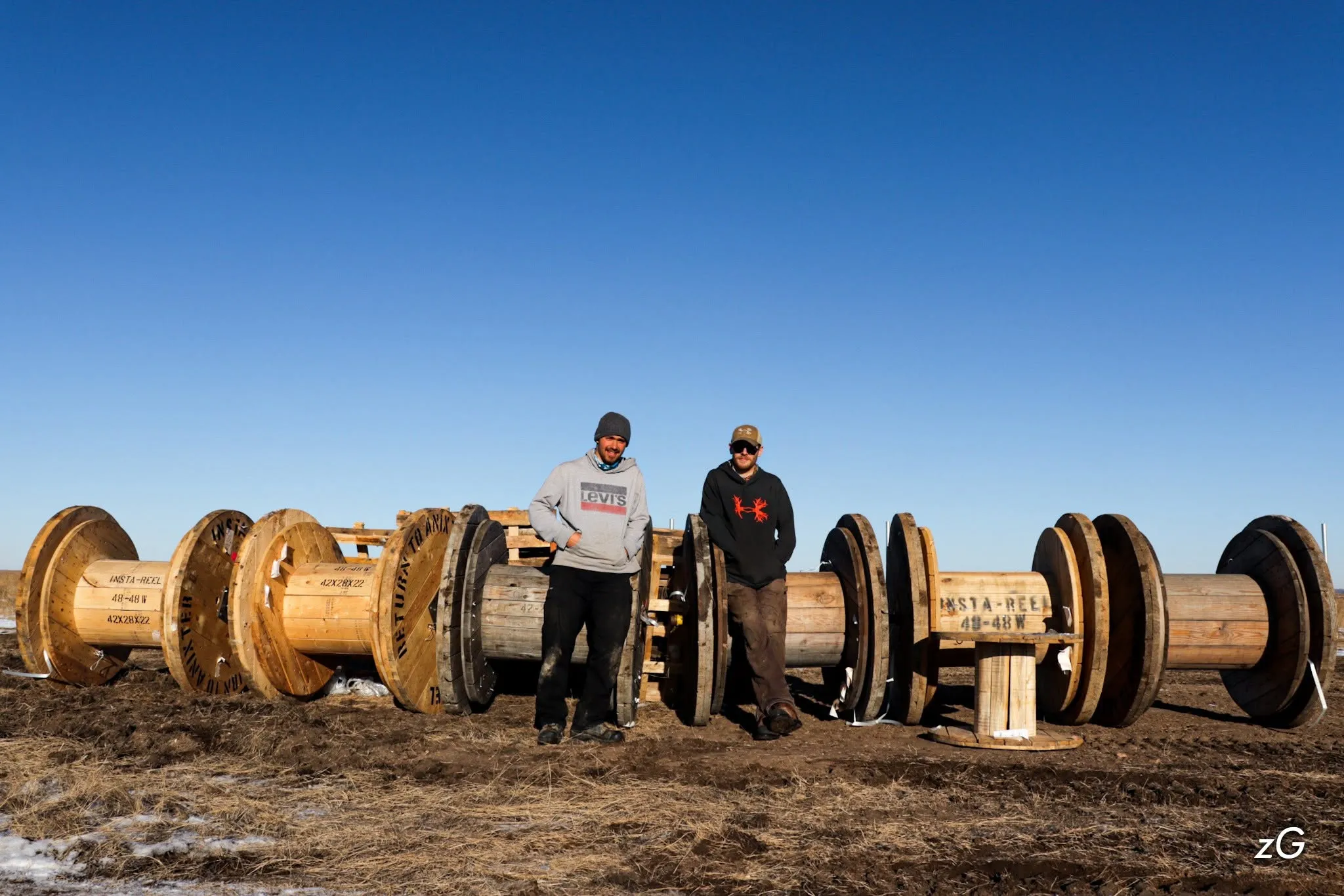 Two CL Electric electricians standing with cable reels on a rural project near Saskatoon