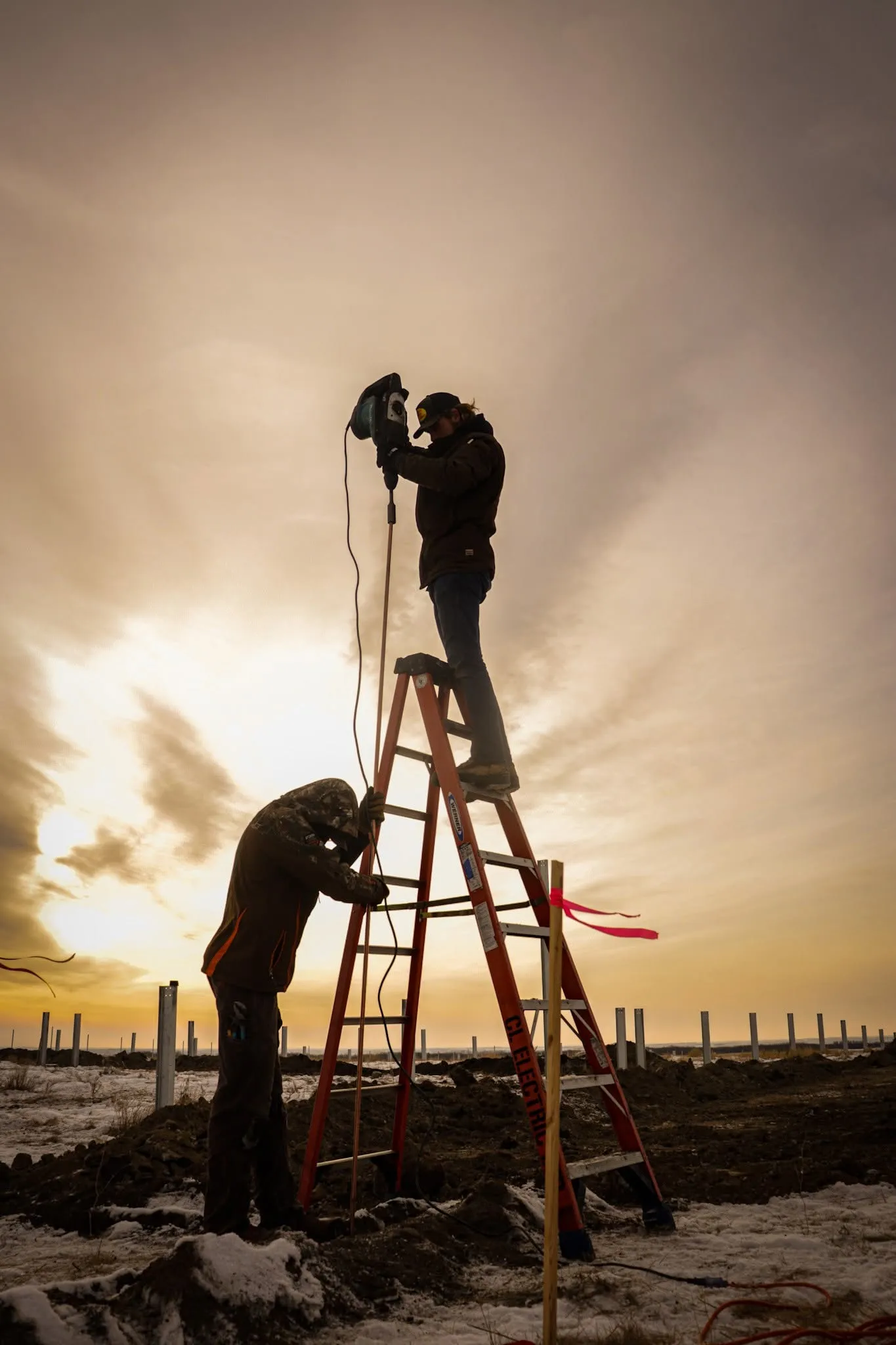 CL Electric crew working from a ladder at sunset on a rural Saskatchewan job site