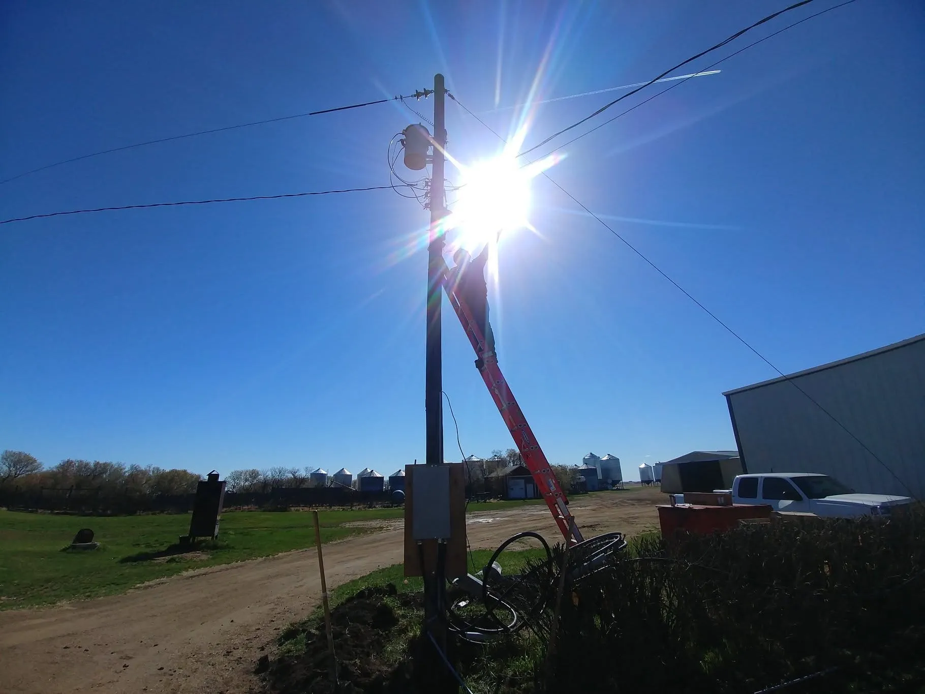 Overhead electrical service being upgraded at a rural yard site, sun behind the pole